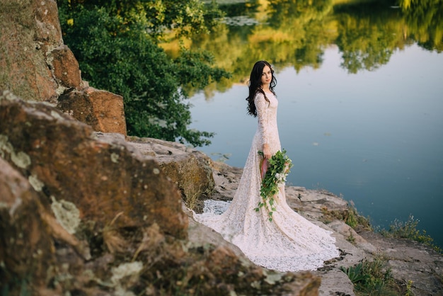 Young bride standing on rocky river bank, sunset