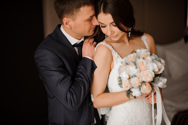 Young bridegroom gently hugs his charming bride with a bouquet