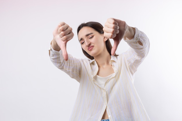 Young brunette in a blue tank top giving thumb down gesture looking with negative expression