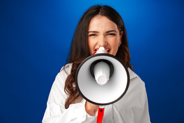 Young brunette businesswoman holding a megaphone against blue background