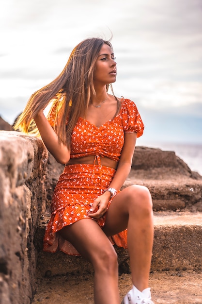 A young brunette Caucasian woman in a red dress on the beach of Itzurrun in the town of Zumaia, Gipuzkoa. Basque Country. Lifestyle session, enjoying the sea on the stairs looking to the right