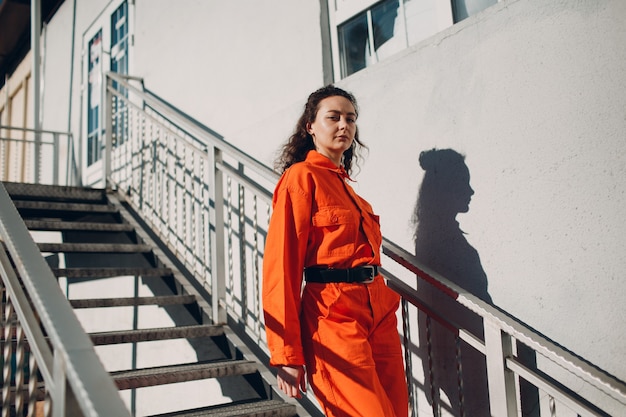 Young brunette curly woman in orange suit. Female in colorful overalls portrait.