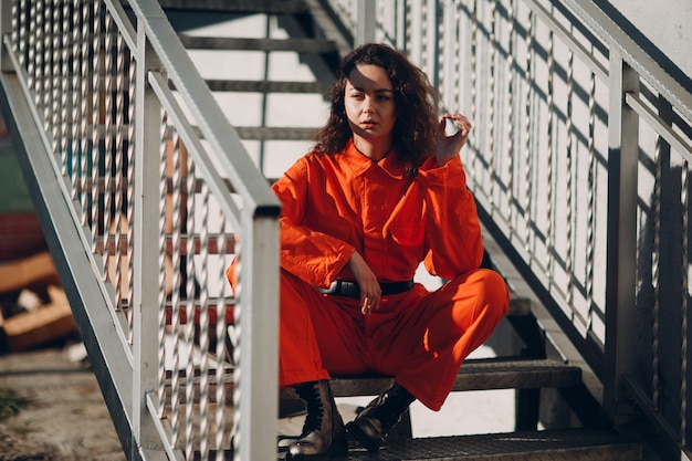 Young brunette curly woman in orange suit. Female in colorful overalls portrait.