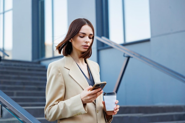 A young brunette girl against the backdrop of a business center office center On the go he reads the news from his smartphone