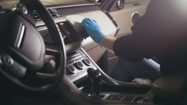 Young brunette girl in gloves is washing with brush a car dashboard and steering wheel, profile view