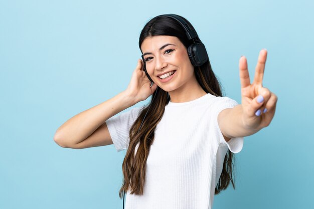 Young brunette girl over isolated blue listening music and singing