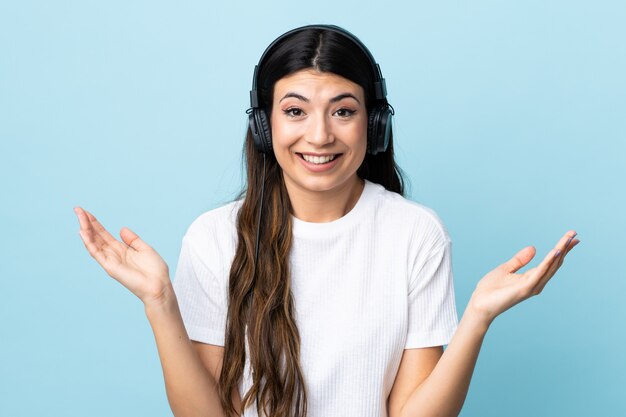 Young brunette girl over isolated blue wall surprised and listening music