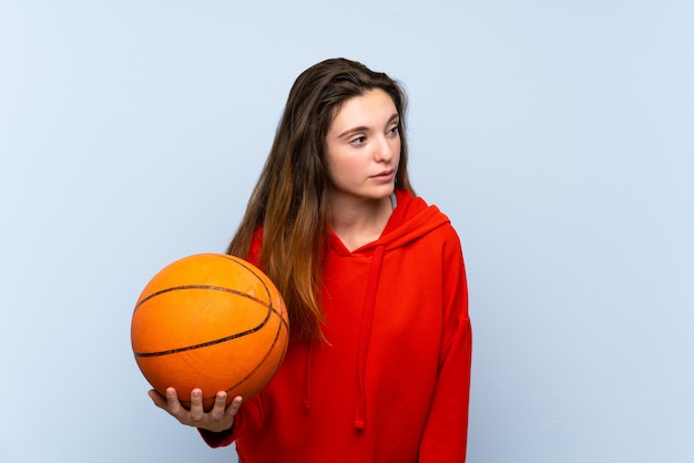 Young brunette girl over isolated blue wall with ball of basketball