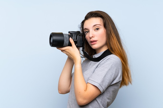 Young brunette girl over isolated blue wall with a professional camera