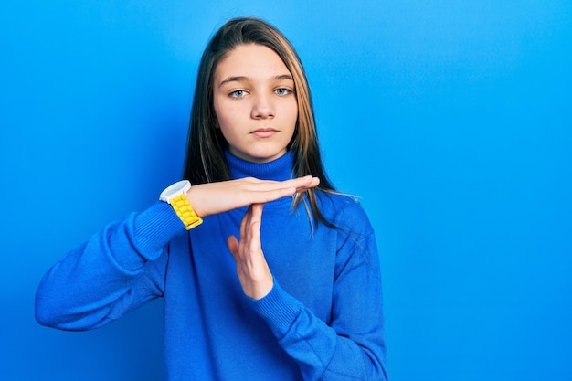 Young brunette girl wearing turtleneck sweater doing time out gesture with hands frustrated and serious face