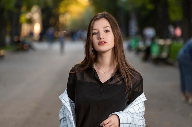 Young brunette girl with brown eyes and beautiful skin in the background of the park Portrait of sexy ravenhaired