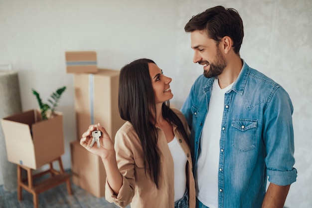 Young brunette lady looking at her male partner with love and affection while holding metal keys from a house