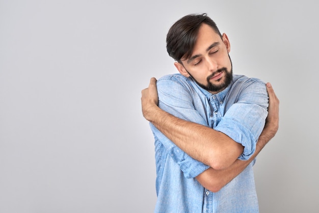 Young brunette male hugging himself and smiling isolated on white studio background self love and self care concept