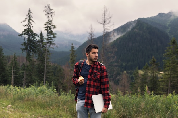 Young brunette male in jeans and shirt is working at a computer while being on the nature. 