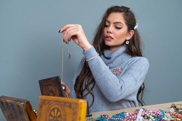 Young brunette sitting at the table with lots of jewelry choosing and trying different jewelry