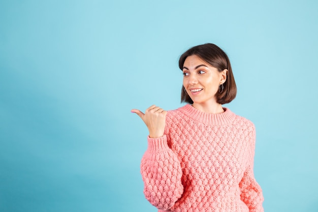 Young brunette in warm pink sweater isolated on blue wall