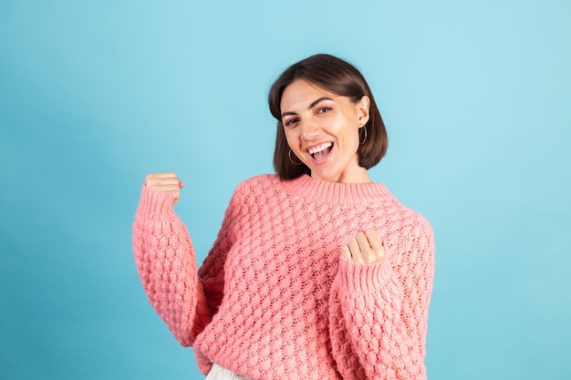 Young brunette in warm pink sweater isolated on blue wall