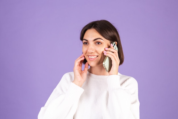 Young brunette in white casual sweater isolated on purple wall