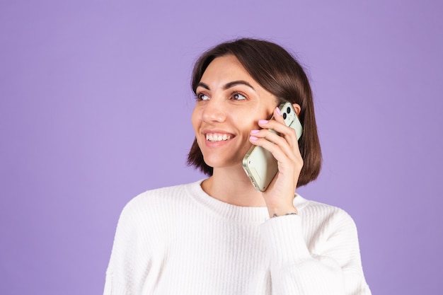 Young brunette in white casual sweater isolated on purple wall