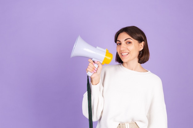 Young brunette in white casual sweater isolated on purple wall