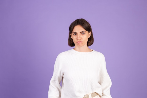 Young brunette in white casual sweater isolated on purple wall