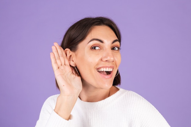 Young brunette in white casual sweater isolated on purple wall