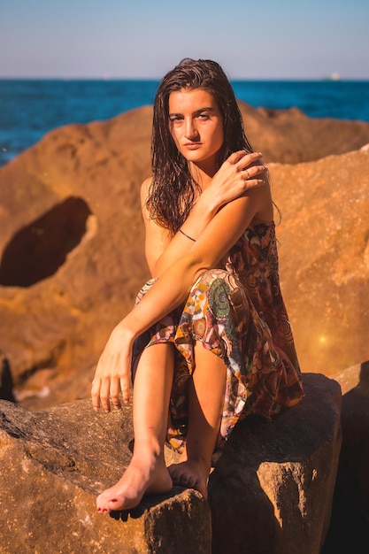 A young brunette with wet hair and a floral dress by the sea summer llifestyle