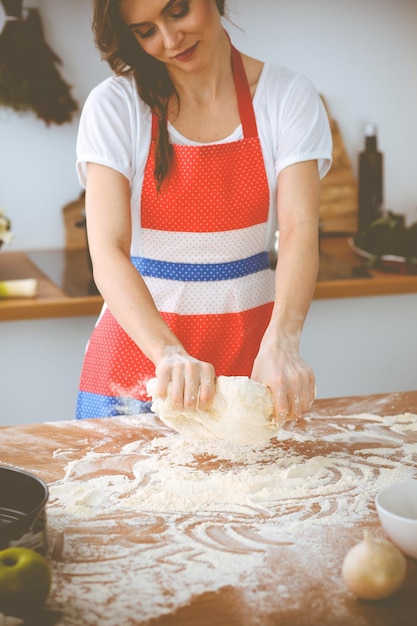 Young brunette woman cooking pizza or handmade pasta in the kitchen. Housewife preparing dough on wooden table. Dieting, food and health concept.