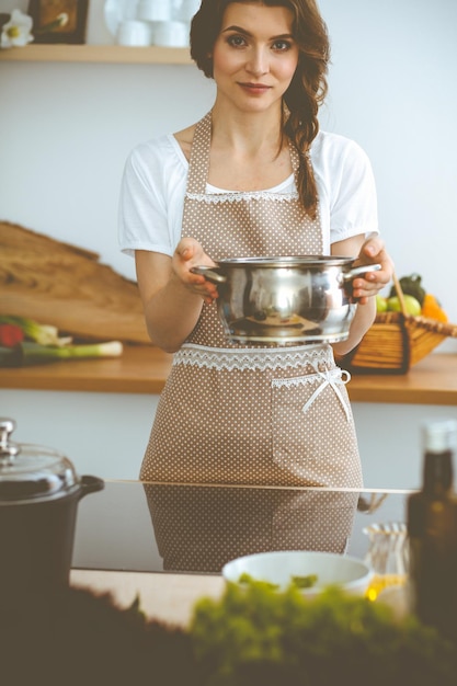 Young brunette woman cooking soup in kitchen. Food and health concept.