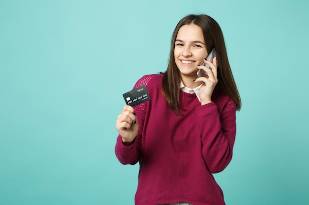 Young brunette woman girl in casual clothes posing isolated on blue background studio portrait. People sincere emotions lifestyle concept. Mock up copy space Hold in hand credit bank card mobile phone