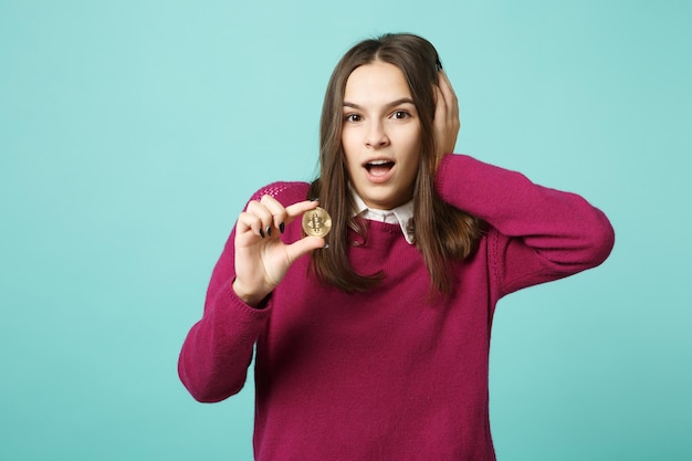 Young brunette woman girl in casual clothes posing isolated on blue green turquoise wall background studio portrait. People sincere emotions lifestyle concept. Mock up copy space. hold in hand bitcoin