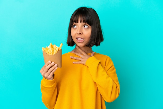 Young brunette woman holding fried chips over isolated blue background looking up while smiling