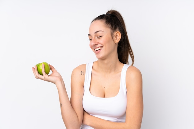 Young brunette woman over isolated white wall with an apple and happy