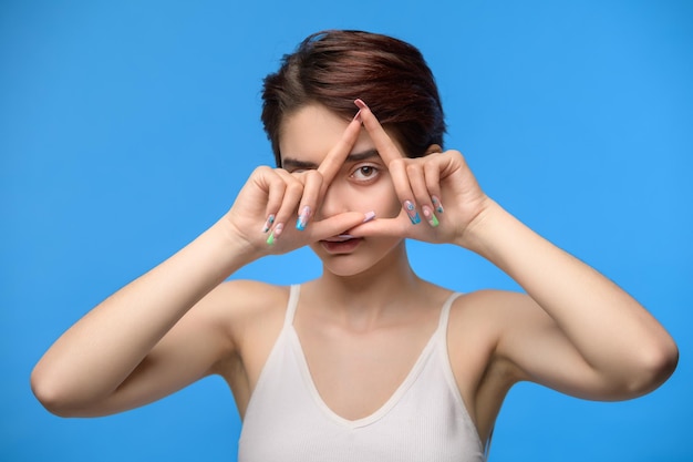 Young brunette woman looking through triangle finger frame