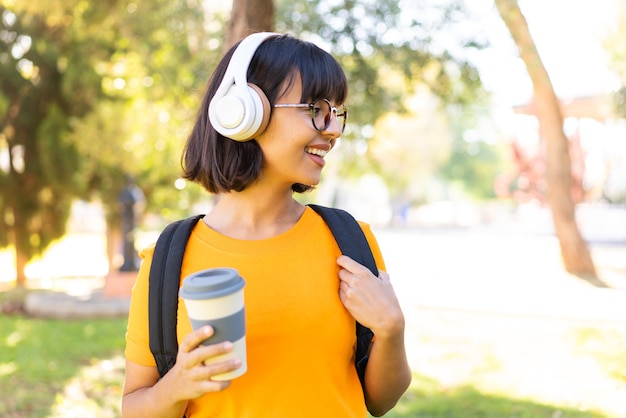 Young brunette woman at outdoors listening music and holding a take away coffee