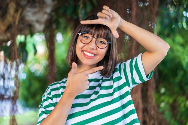 Young brunette woman at outdoors in a park focusing face. Framing symbol