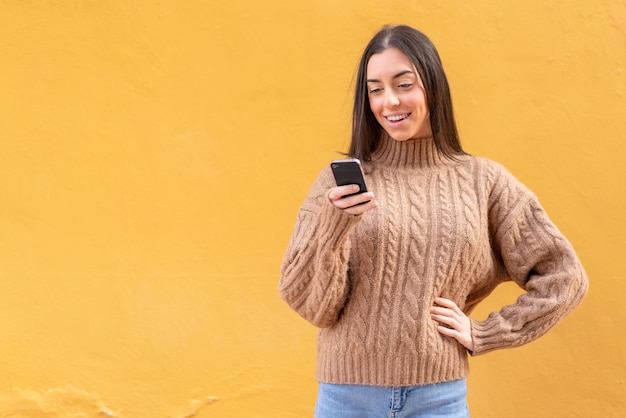 Young brunette woman at outdoors sending a message or email with the mobile