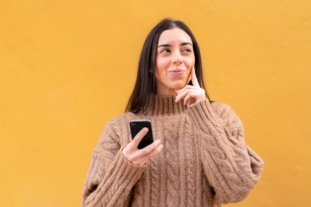 Young brunette woman at outdoors using mobile phone and thinking