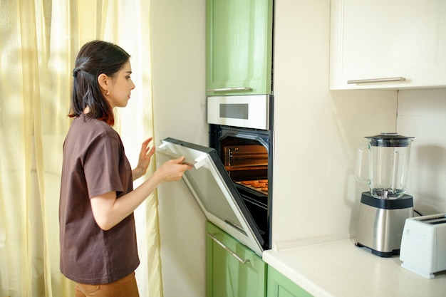 Young brunette woman preparing homemade cakes in a modern builtin oven