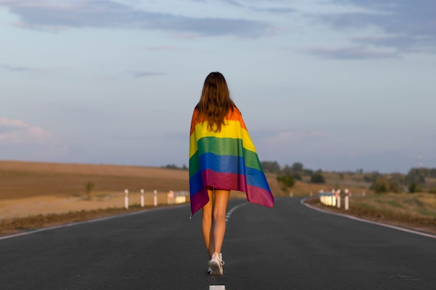 Young brunette woman walking down the road covering with lgbt pride flag LGBT flag