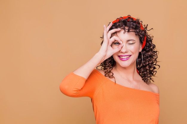 Young brunette woman wearing bandana and orange blouse doing ok gesture with hand smiling