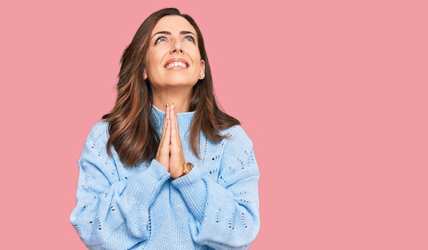 Young brunette woman wearing casual winter sweater begging and praying with hands together with hope expression on face very emotional and worried. begging.