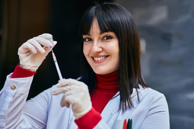 Young brunette woman wearing doctor uniform holding syringe and vaccine at the city