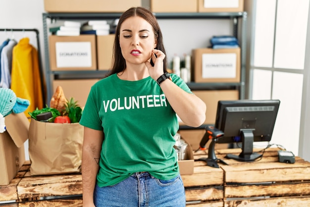 Young brunette woman wearing volunteer t shirt at donations stand touching mouth with hand with painful expression because of toothache or dental illness on teeth. dentist concept.