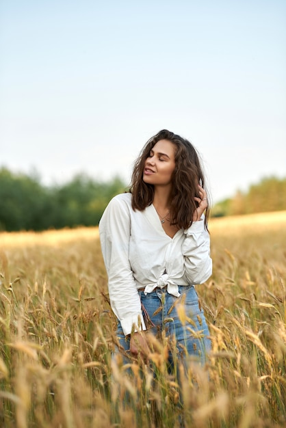 young brunette woman in white shirt and blue jeans  on a background of golden wheat field