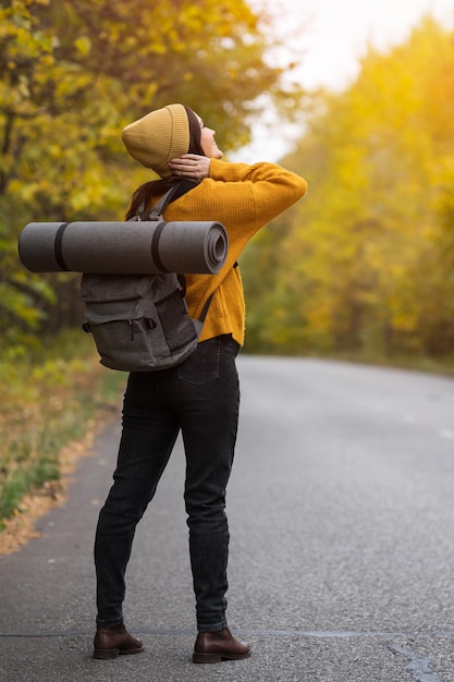 Young brunette woman with backpack stands on autumn road