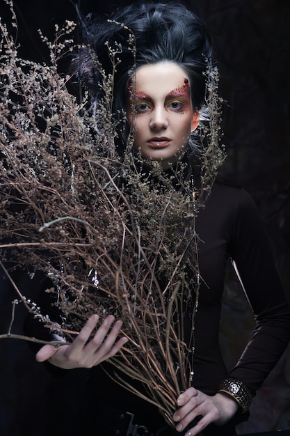 Young brunette woman with bright make up with dry branches