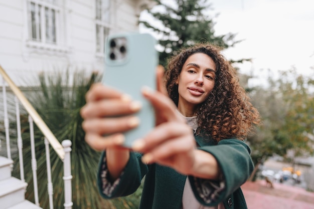 Young brunette woman with curly hair taking a photo over street