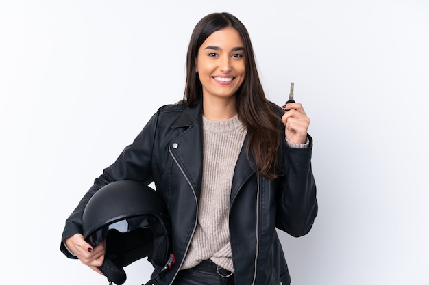 Young brunette woman with a motorcycle helmet and holding a key over isolated white wall