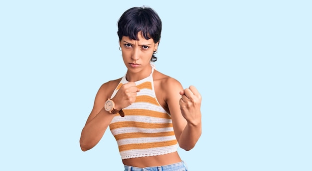 Young brunette woman with short hair wearing casual clothes ready to fight with fist defense gesture angry and upset face afraid of problem